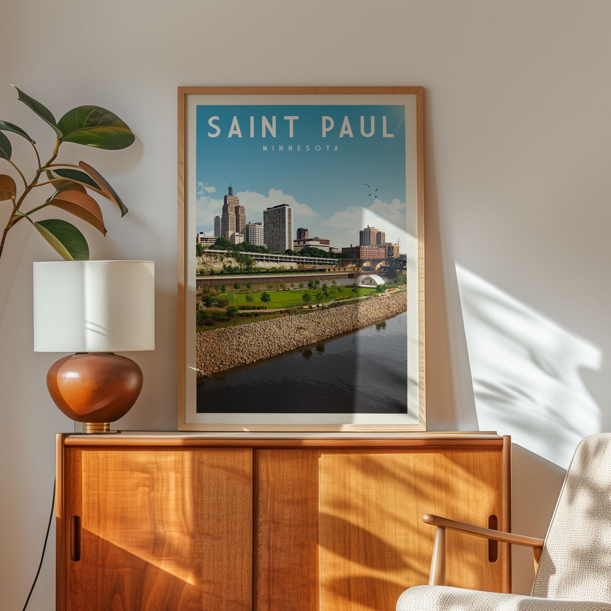 a framed poster of the Saint Paul, Minnesota skyline, with a wooden cabinet and a lamp in the foreground.