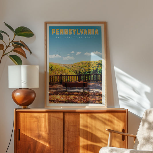a framed poster of a scenic outdoor landscape with a bench and a wooden fence, hanging on a wall above a wooden cabinet.