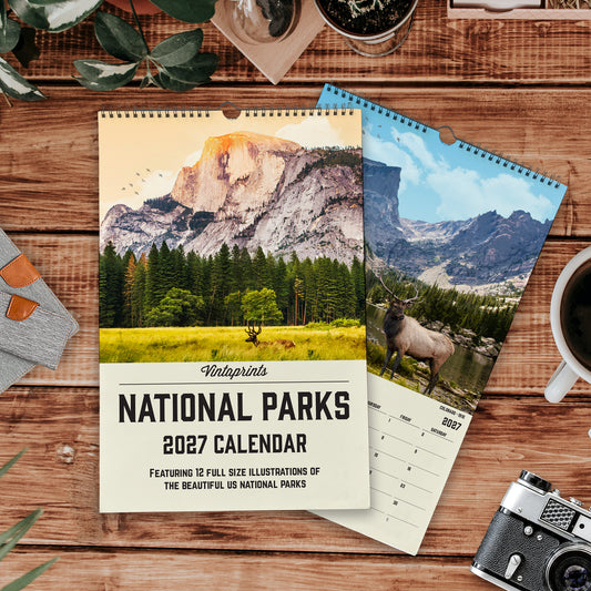 a calendar for National Parks, with a scenic mountain landscape on the cover and a smaller calendar below it. The calendar is placed on a wooden surface, surrounded by various items such as a camera, a cup, and some plants.