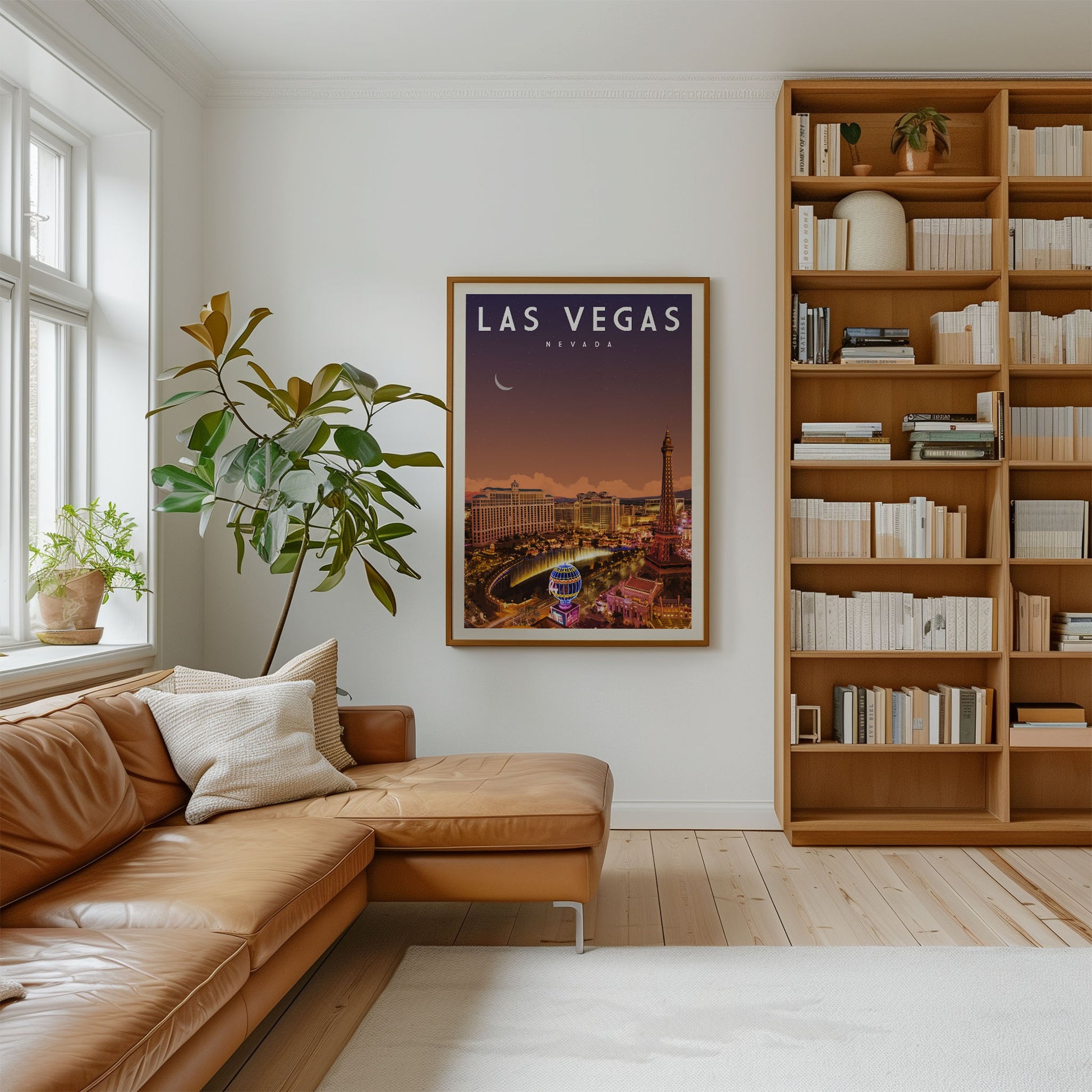 a living room with a large framed poster of Las Vegas on the wall, a brown leather sofa, a wooden bookshelf filled with books, and a potted plant.