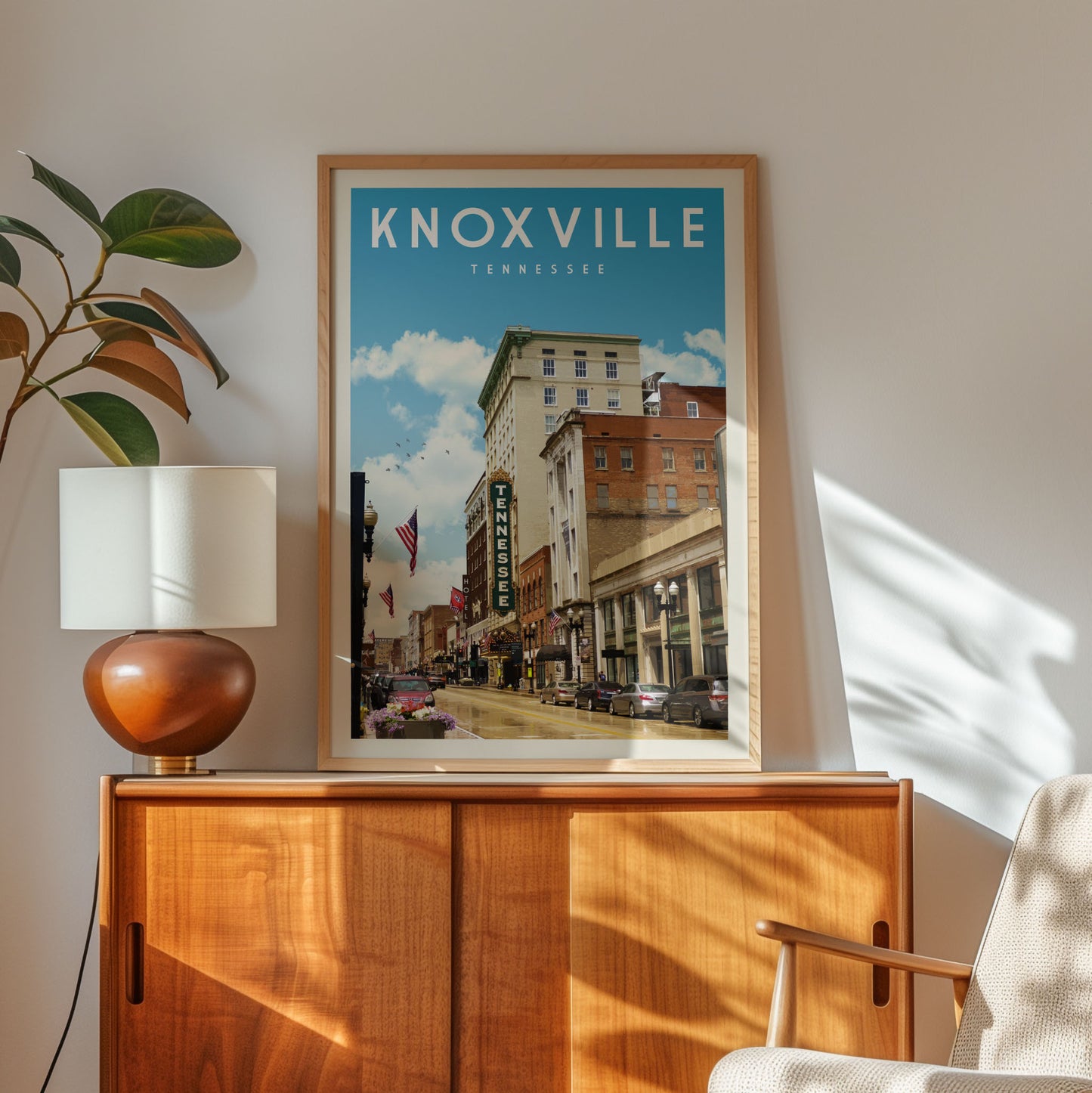 a framed poster of a cityscape with buildings and a street, hanging on a wall above a wooden cabinet.