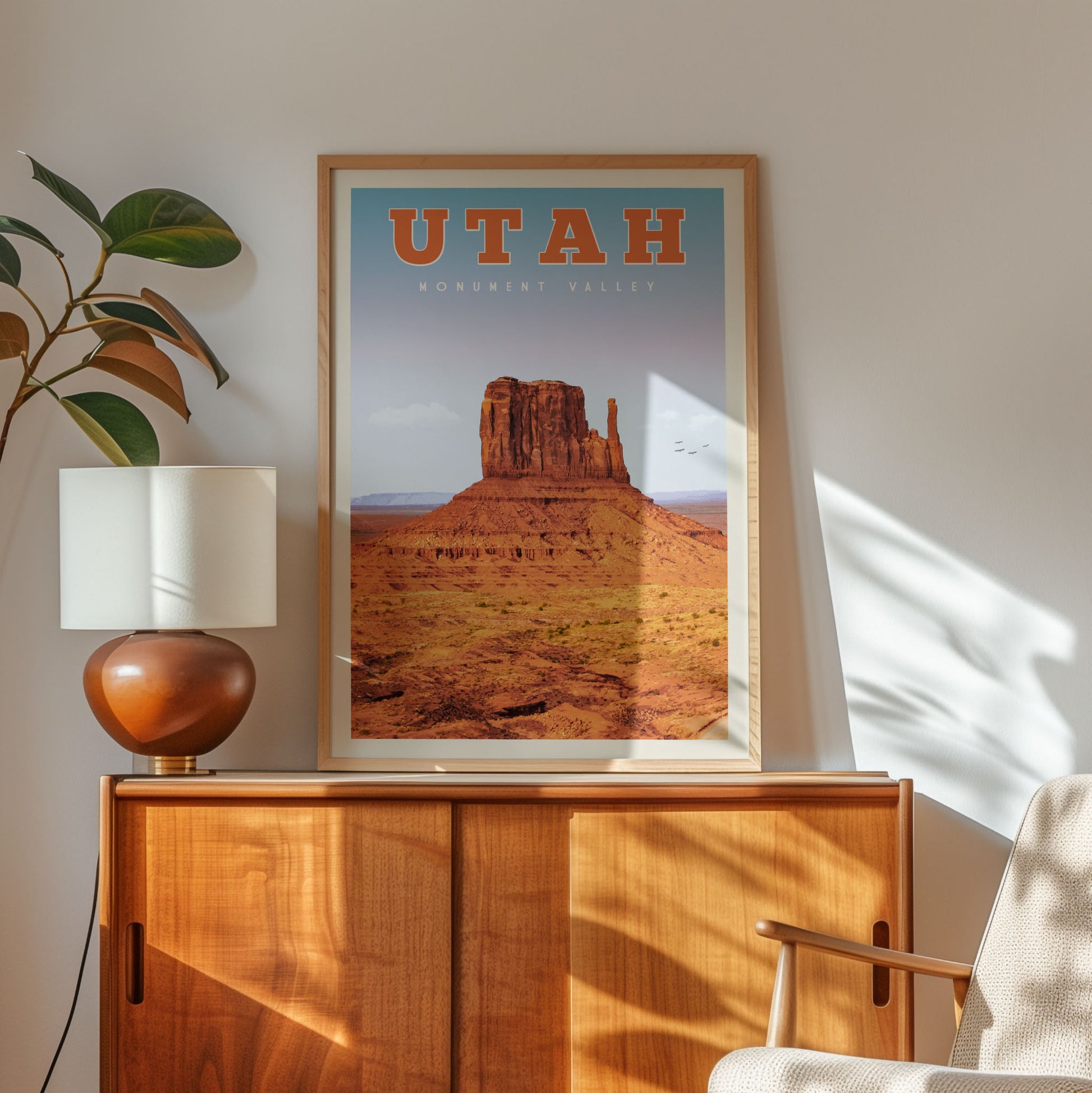 A framed poster of Monument Valley hangs on a wall, with a wooden cabinet below it and a plant to the left.