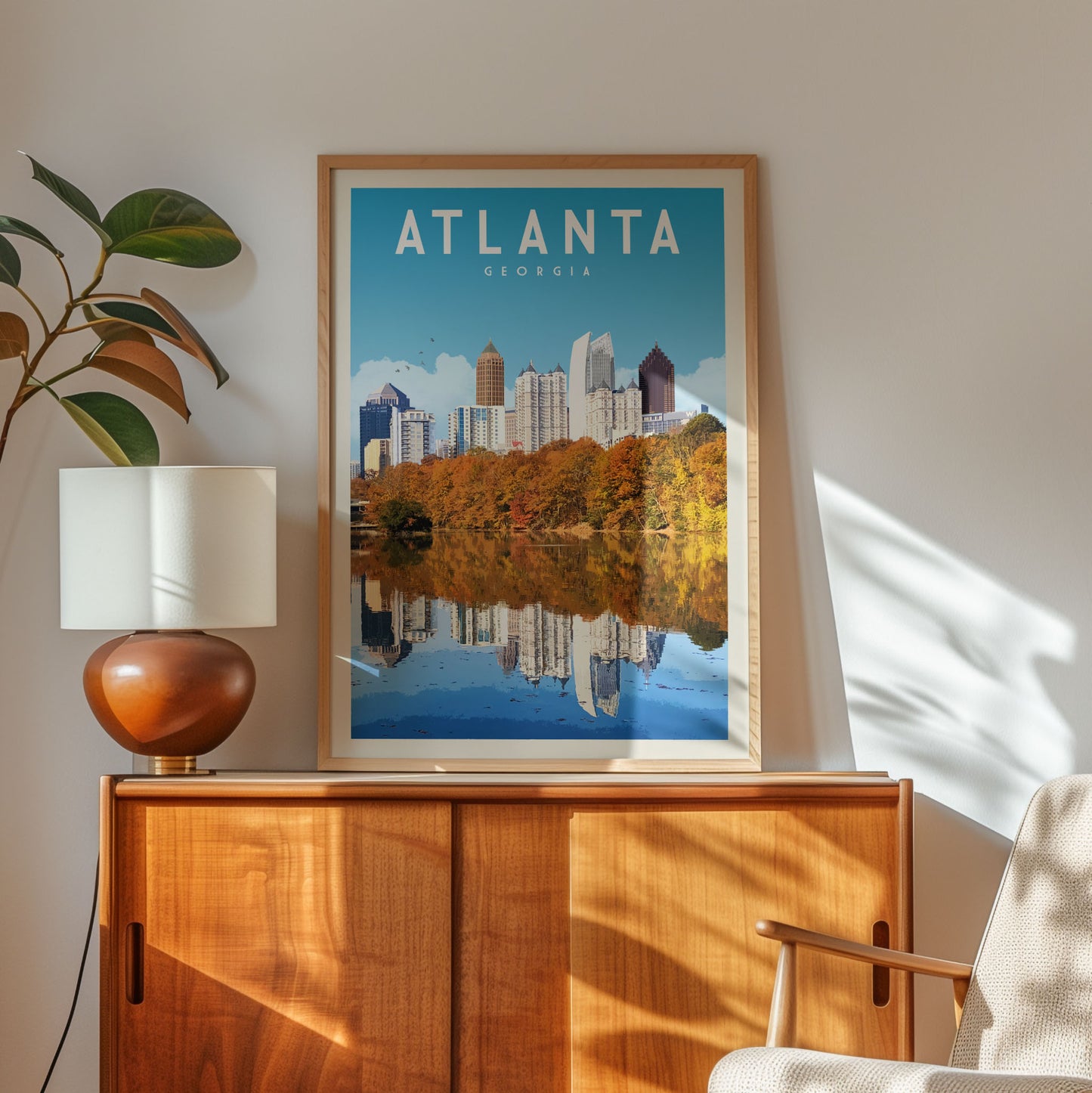 a framed poster of Atlanta, Georgia, with a cityscape and a lake in the background, displayed on a wooden cabinet.