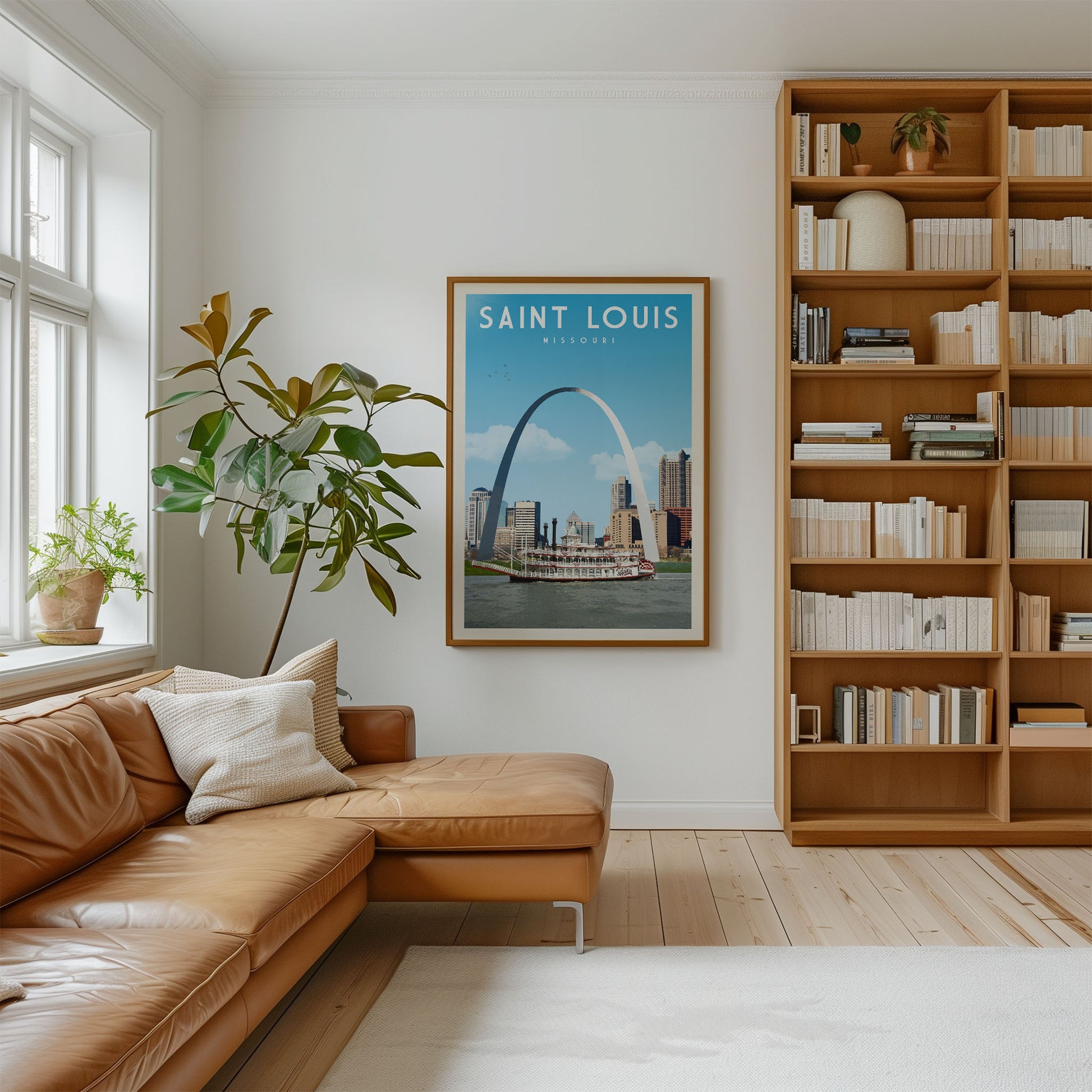 a cozy living room with a large window, a brown leather sofa, a framed poster of the St. Louis arch, and a bookshelf filled with books.