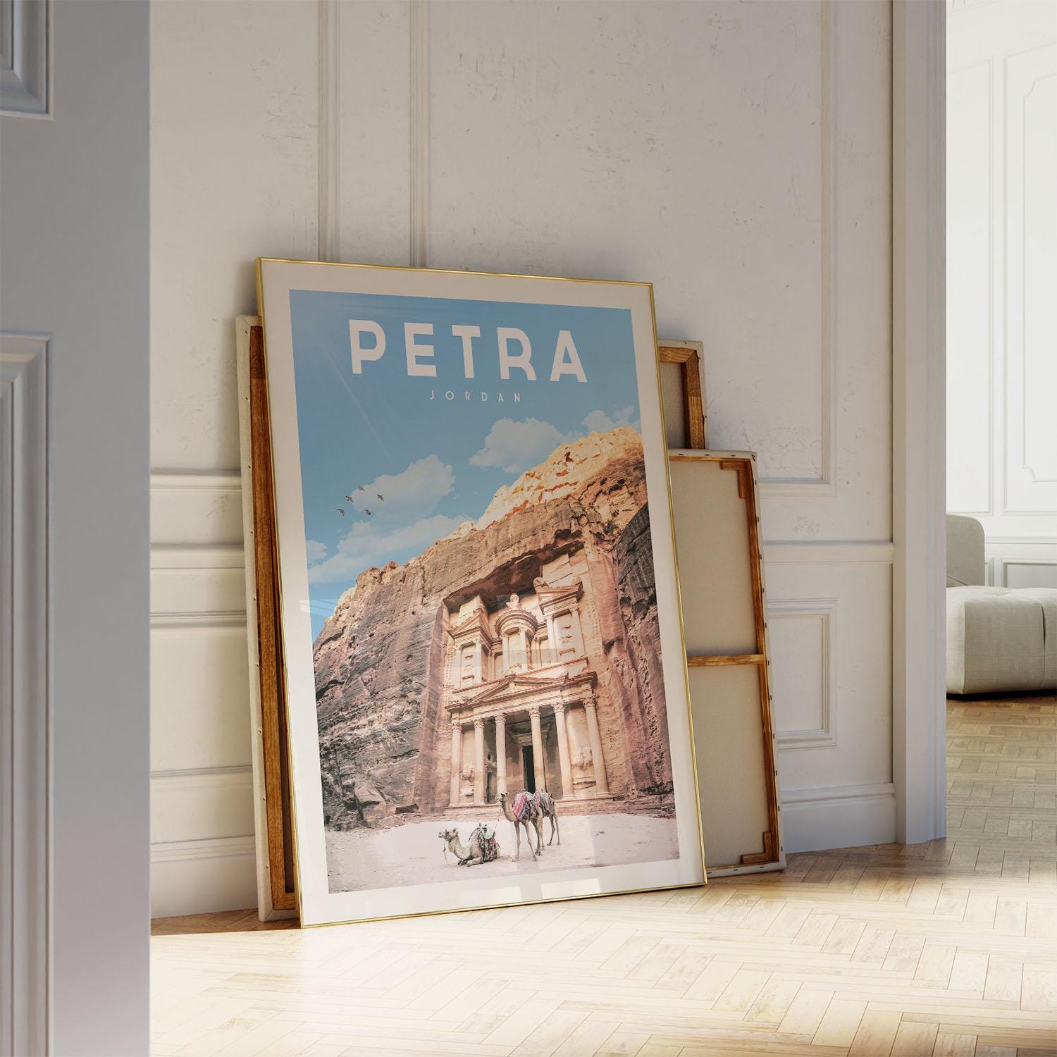 A framed poster of the ancient city of Petra, featuring the iconic rock-cut architecture of the Treasury of the Kings, is leaning against a white wall.