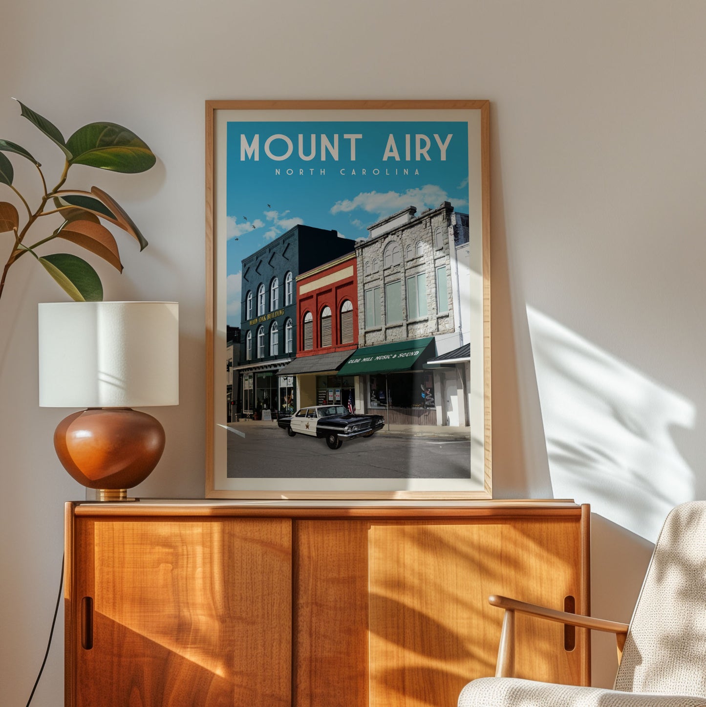 a framed poster of a street scene in Mount Airy, North Carolina, with a car parked on the street and buildings in the background.