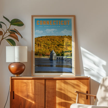 a framed poster of a scenic landscape with a lake and a bridge, hanging on a wall next to a wooden cabinet and a lamp.