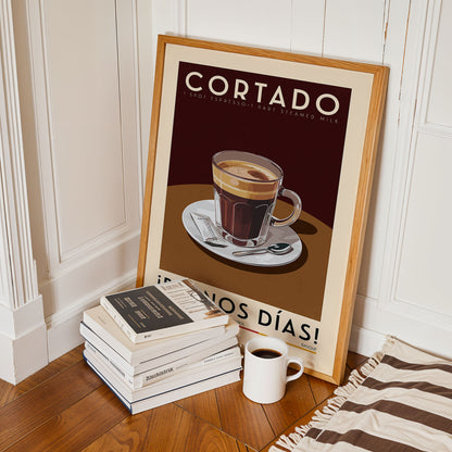a framed poster of a cup of coffee with the text "CORTADO" and "I'M NOT EXPLOITING" on it, along with a stack of books and a white mug on a wooden floor.