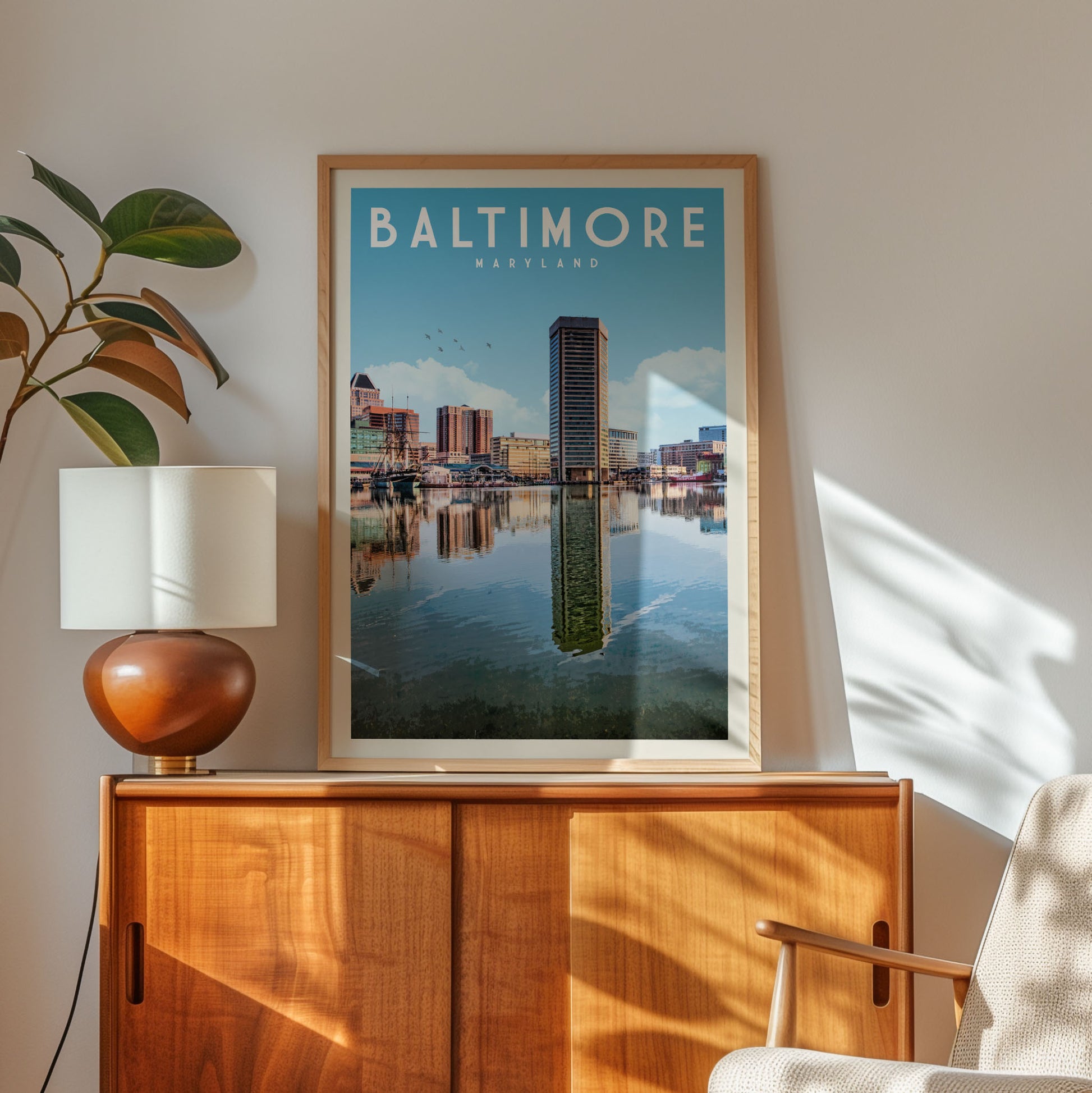 a framed poster of Baltimore, Maryland, with a cityscape and a body of water in the background. The poster is displayed on a wooden cabinet, and there is a lamp and a plant nearby.
