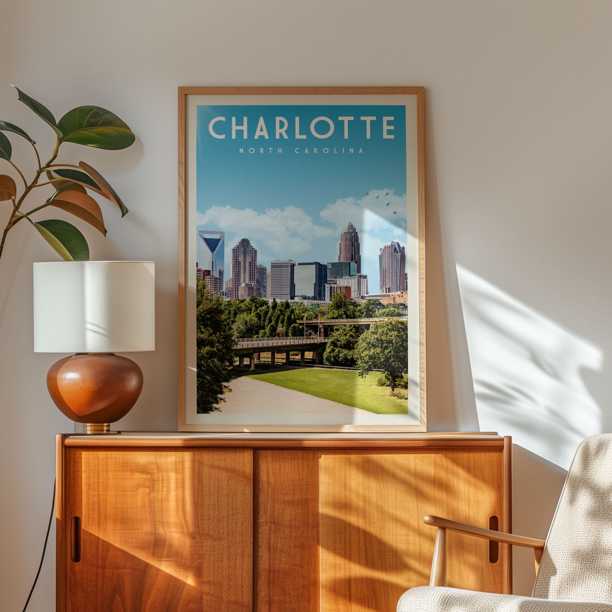 a framed poster of the Charlotte, North Carolina skyline, with a cityscape and a bridge visible, hanging on a wall above a wooden cabinet.