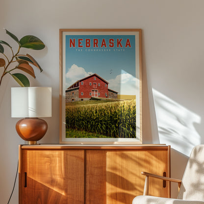 a framed poster of a red barn with a cornfield in the background, hanging on a wall next to a wooden cabinet and a lamp.