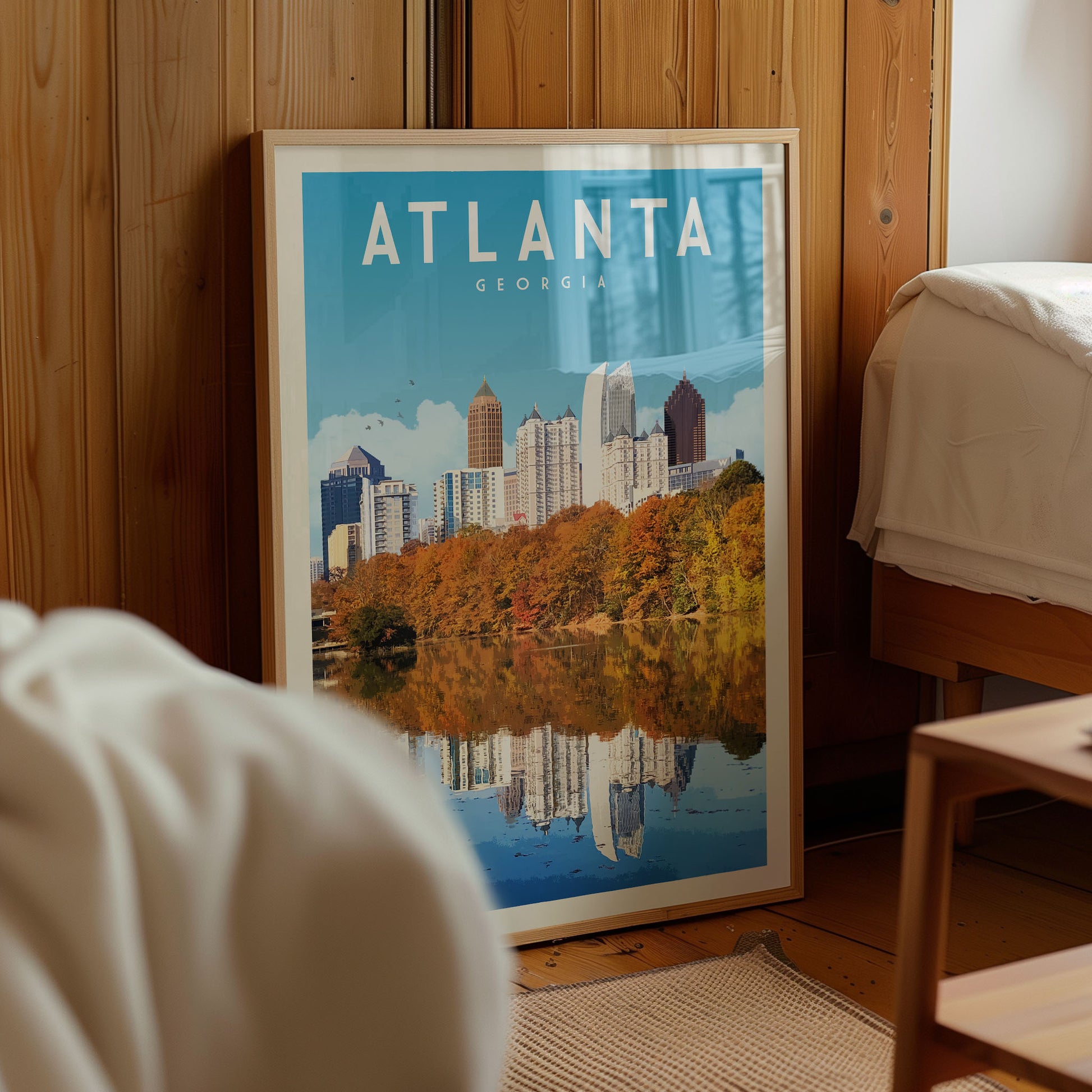 A framed poster of the Atlanta skyline, featuring the city's iconic buildings and trees reflected in a body of water.