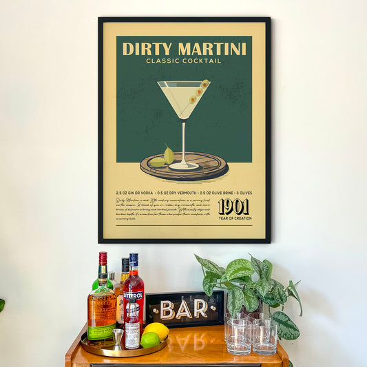 a framed poster of a Dirty Martini cocktail hanging on a wall above a wooden bar counter with various liquor bottles and glasses.