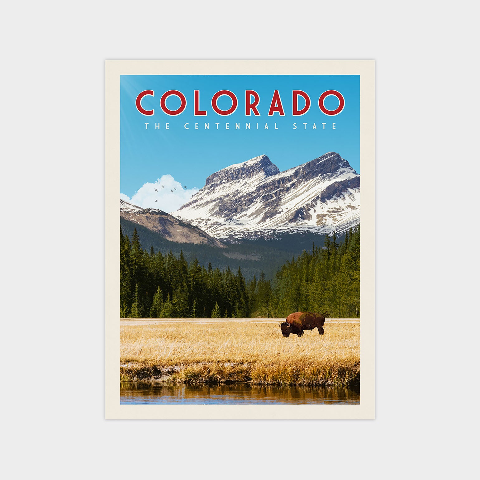 A scenic image of a bison grazing in a field with snow-capped mountains in the background, set against a clear blue sky.