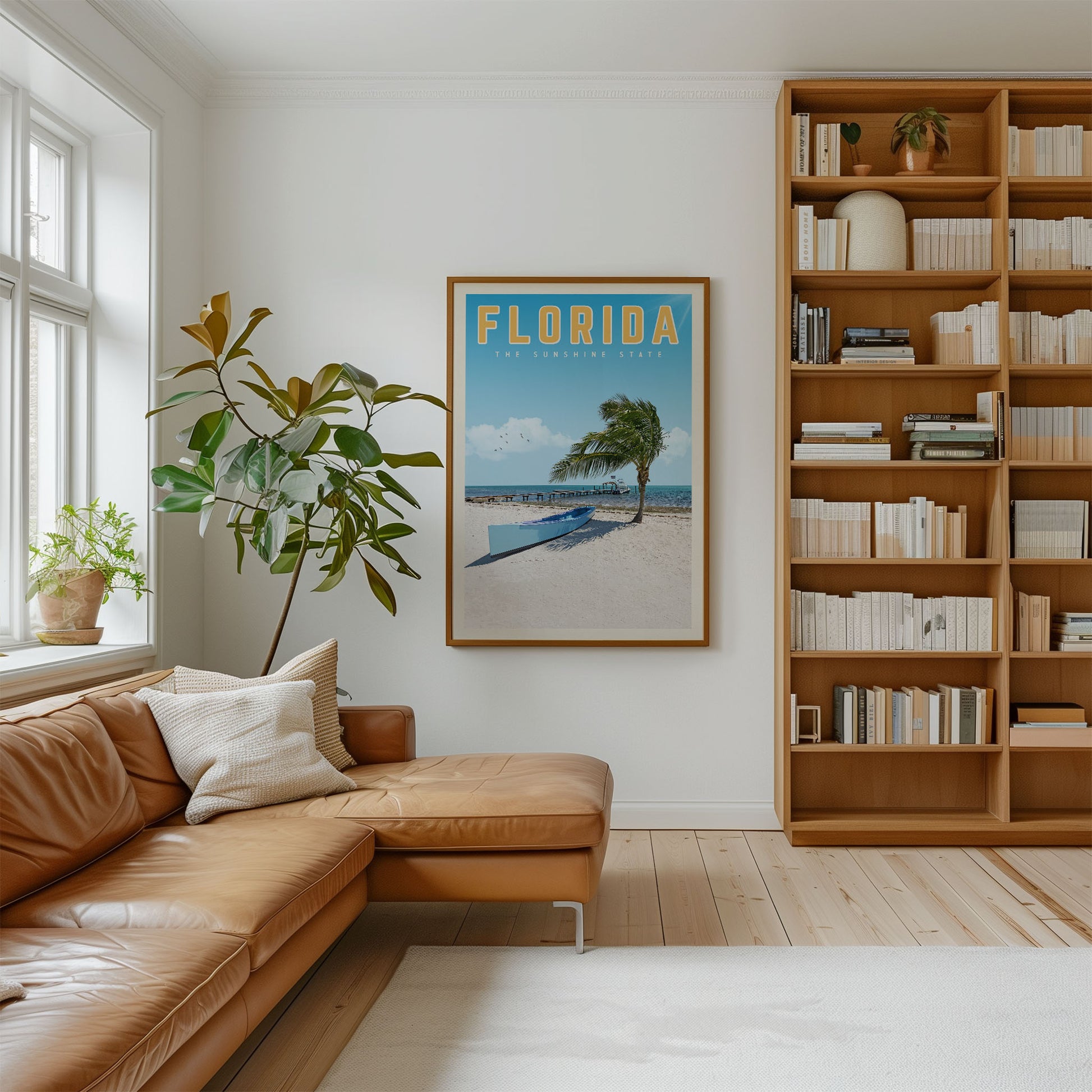 a cozy living room with a large window, a comfortable leather couch, a bookshelf filled with books, and a framed poster of a beach scene hanging on the wall.